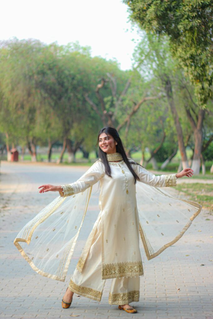 Stylish woman in a traditional beige dress gracefully posing in a serene park setting.
